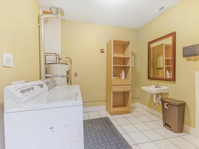 Utility room featuring a built-in water heater, wall-mounted sink, and a mirrored vanity
