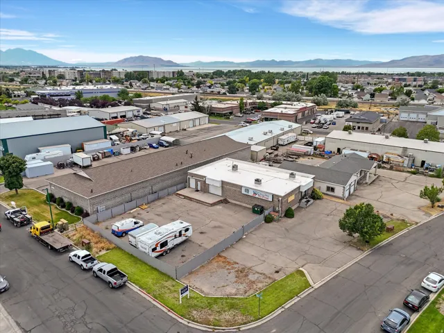 Commercial buildings with multiple rooflines, a large paved lot, and a mountain and water background