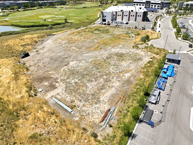 Expansive land parcel featuring partial clearing, surrounding undeveloped terrain, a paved road, and a commercial structure in the background