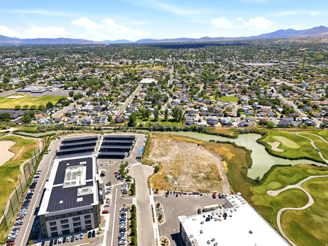 Aerial perspective showcasing a mixed-use development with solar panel covered parking, adjacent to a golf course and residential areas, framed by distant mountains