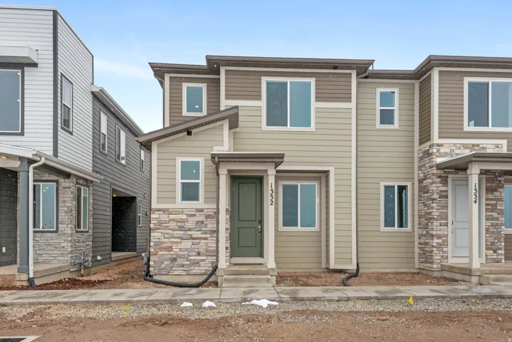 Contemporary townhome featuring a multi-toned facade, decorative stone accents, a covered entry, and multiple windows