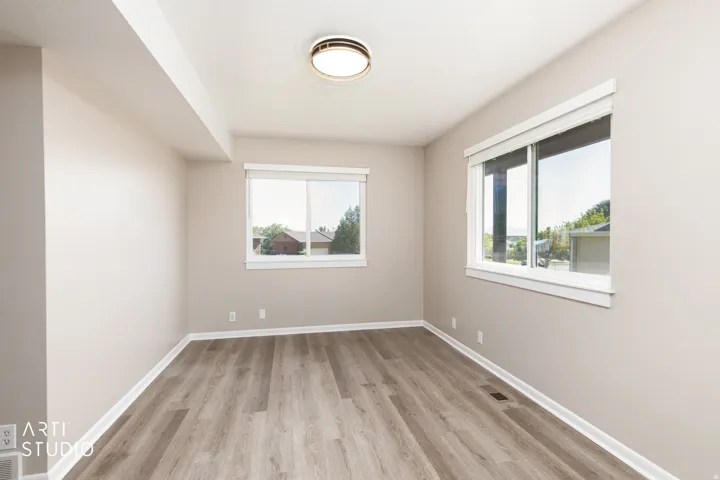 Spacious room featuring wood-finish flooring, two large windows with white trim, a flush-mount ceiling light fixture, and neutral painted walls