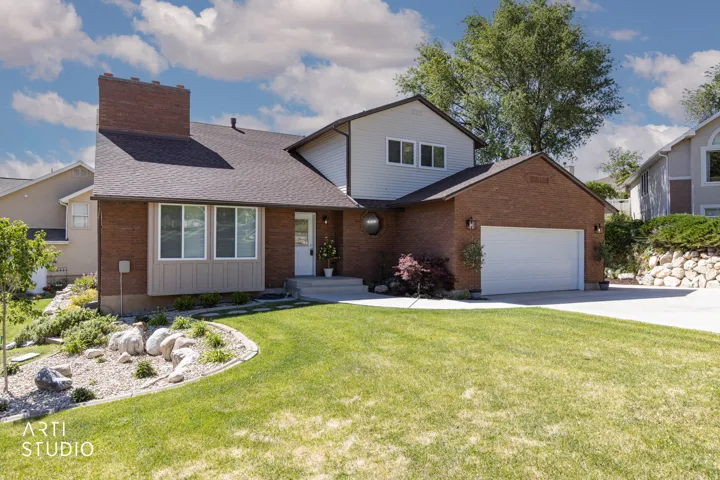 Brick and siding exterior featuring a prominent chimney, a two-car garage, and a concrete driveway