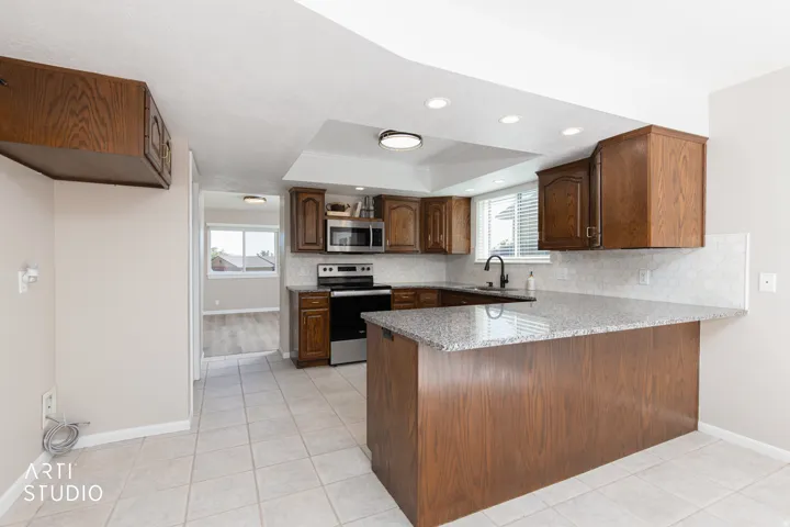 Kitchen featuring wood-finish cabinetry, granite-style countertops, stainless steel appliances, a tile backsplash, and recessed lighting