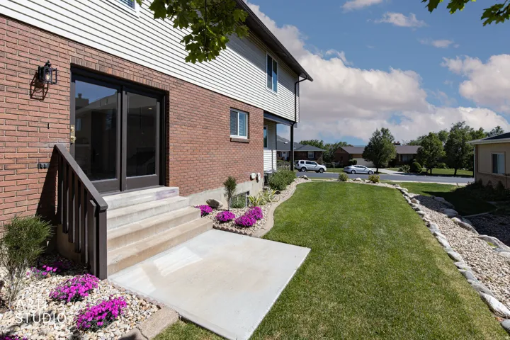 Rear exterior featuring brick and siding finishes, a lower-level patio with steps, and a grass lawn