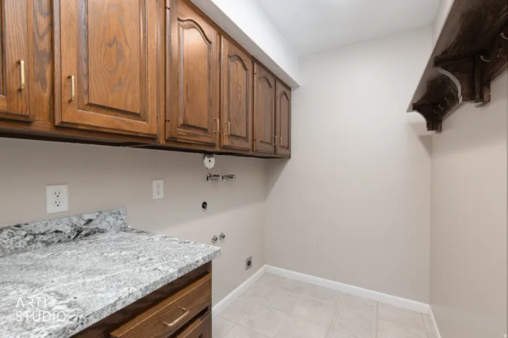 Laundry area featuring wood cabinetry with gold-tone hardware, a light-toned speckled countertop, and tiled flooring