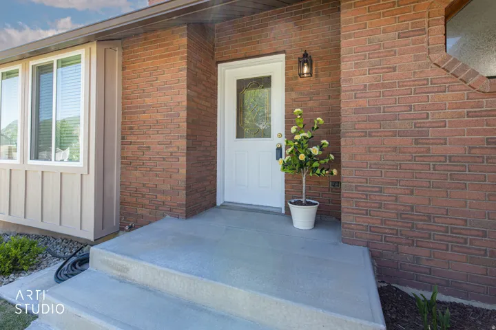 Brick exterior with a white entry door featuring decorative glass, a concrete front stoop, and an exterior wall lantern