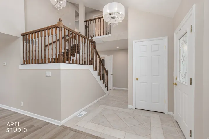 Two-story foyer featuring a grand staircase with wood banisters, decorative tile flooring, high ceilings, and two contemporary chandeliers