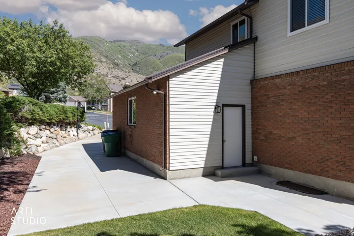 Exterior showcasing brick and siding finishes, a lower-level access door, concrete pathway, and a stone retaining wall