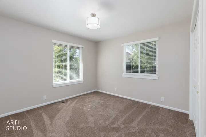 Carpeted room featuring two windows with white blinds, a semi-flush mount ceiling light, and light-toned walls
