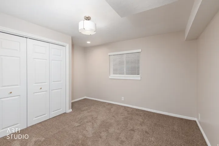 Spacious room featuring neutral carpeting, a dual-door closet with gold-toned knobs, and a window with blinds