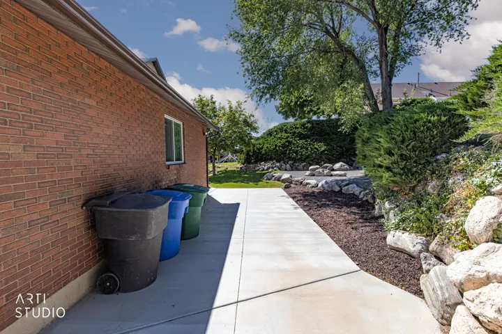 Brick exterior wall featuring a window with white trim, a concrete walkway, and a landscaped garden bed with decorative rocks and foliage