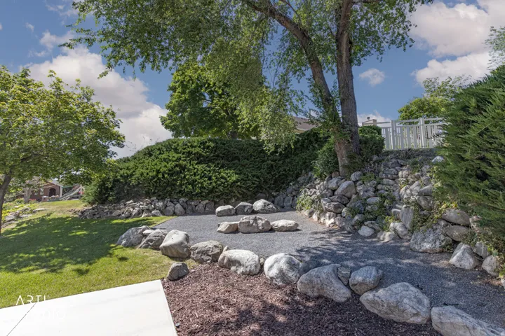 Outdoor entertainment area featuring a gravel-surfaced patio, surrounded by natural boulders, and mulched landscaping