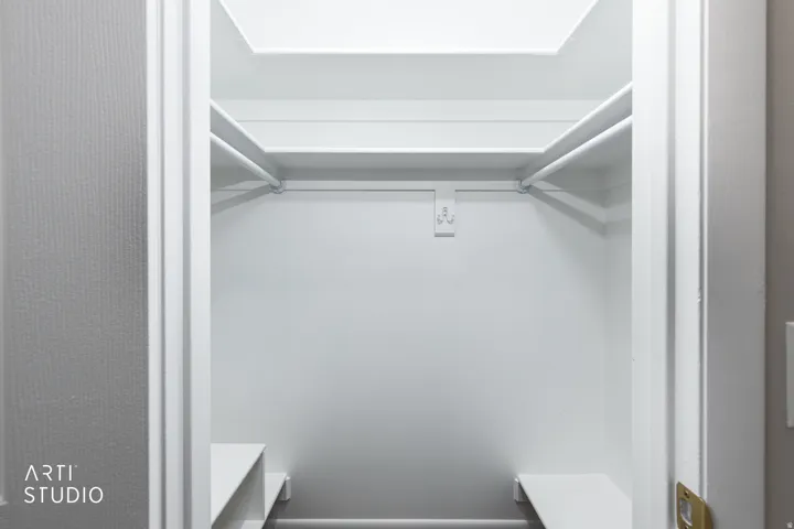 Walk-in closet featuring white painted walls, upper shelving, hanging rods, and lower built-in shelving