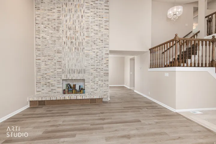 Great room featuring a full-height brick fireplace, wood-finish flooring, high ceilings, and an elegant chandelier