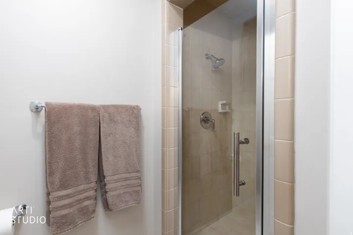 Glass-enclosed shower with ceramic tile surround and a chrome showerhead and fixtures