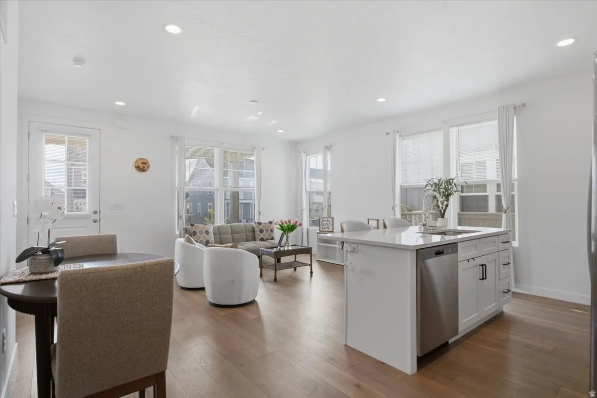 Open-concept living space featuring stainless steel appliances, white cabinetry with integrated storage, wood-finish flooring throughout, recessed ceiling lighting, and expansive windows with natural light and city views