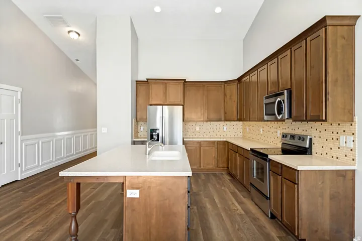 Kitchen featuring wood-finish flooring, light-toned cabinetry, stainless steel appliances, a center island with sink, and light-toned countertops