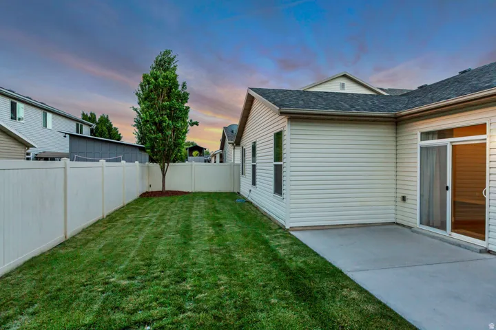 Expansive rear yard featuring a manicured lawn, established tree, and full privacy fencing