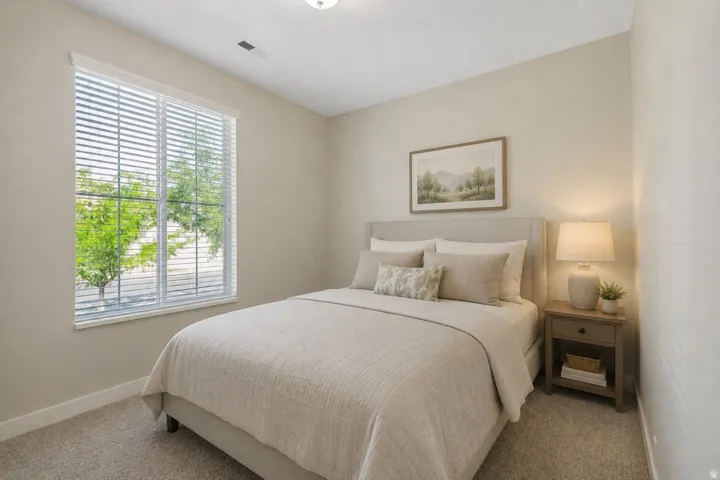Virtualy staged using AI. Carpeted room featuring a large window with horizontal blinds, light-toned walls, and a ceiling light fixture
