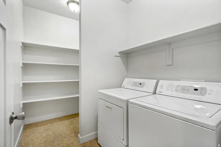 Laundry area featuring a side-by-side washer and dryer, an overhead wall-mounted shelf, and an adjacent built-in shelving unit