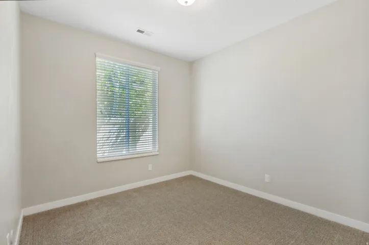Neutral toned room featuring a window with blinds, light tan carpeting, and white baseboards