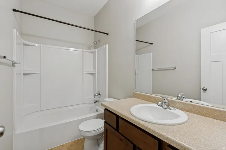 Bathroom featuring a full vanity with an integrated sink, a large wall-mounted mirror, a toilet, and a shower-tub combination with a white surround