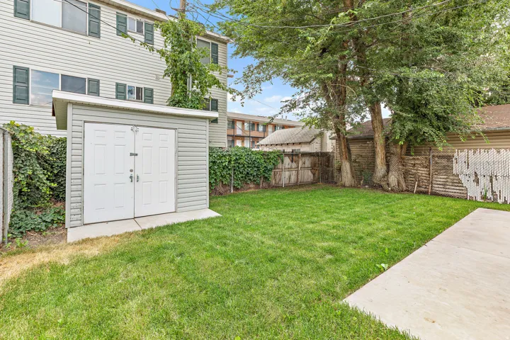 Expansive grassy yard area featuring a storage shed with double doors, mature trees, and concrete paving. Unit 371. 2 bed 1 bath
