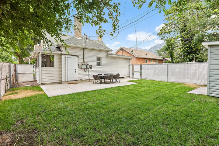 Spacious rear yard featuring a large concrete patio, manicured lawn, and perimeter chain link fencing