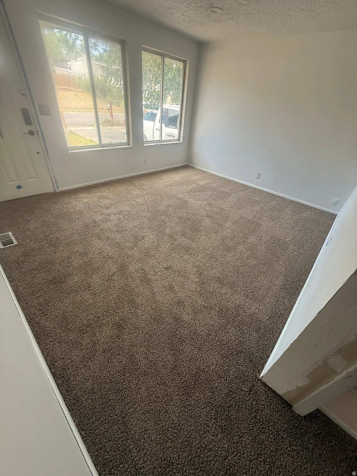 Carpeted living area featuring two large windows,  white entry door with glass window