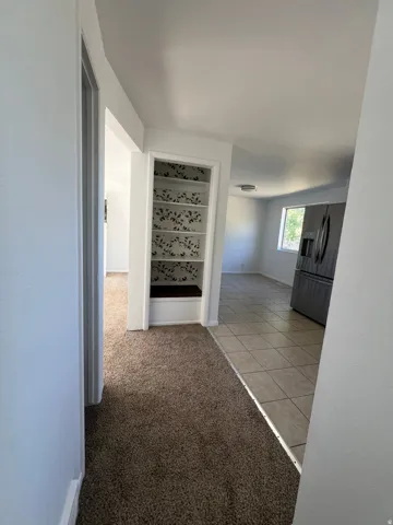 Built-in shelving unit with decorative backing, stainless steel refrigerator, tile flooring, and neutral carpeting