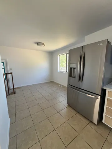 Ceramic tile flooring, stainless steel French door refrigerator, white walls, and a window providing natural light