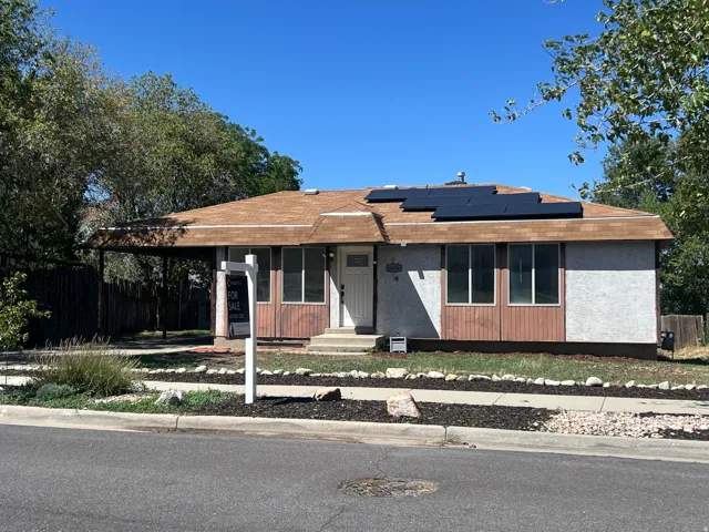 Single-story residence featuring a covered carport, solar panels, and a brown shingle roof