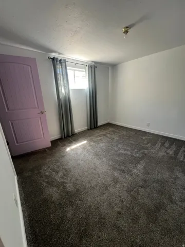White painted walls, dark carpeting, and a window with gray curtains