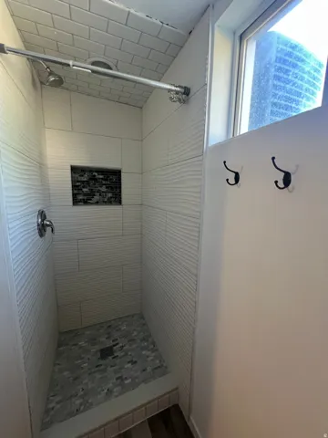 Walk-in shower featuring textured tile walls, mosaic tile shower floor, built-in tile niche, and a chrome shower fixture