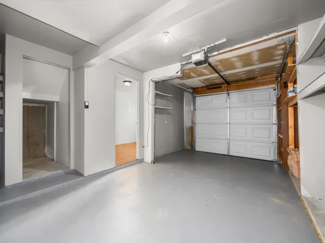 Attached garage with a sectional overhead door, automatic opener, painted concrete flooring, and built-in shelving