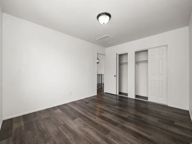 Room featuring wood-finish flooring, two sliding closet doors, and white painted walls