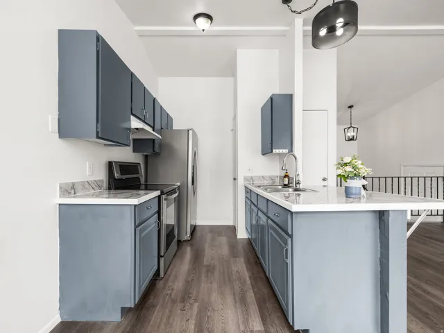 Kitchen featuring slate blue cabinetry, marble-look countertops, stainless steel appliances, wood-finish flooring, and a central island with an undermount sink and gooseneck faucet