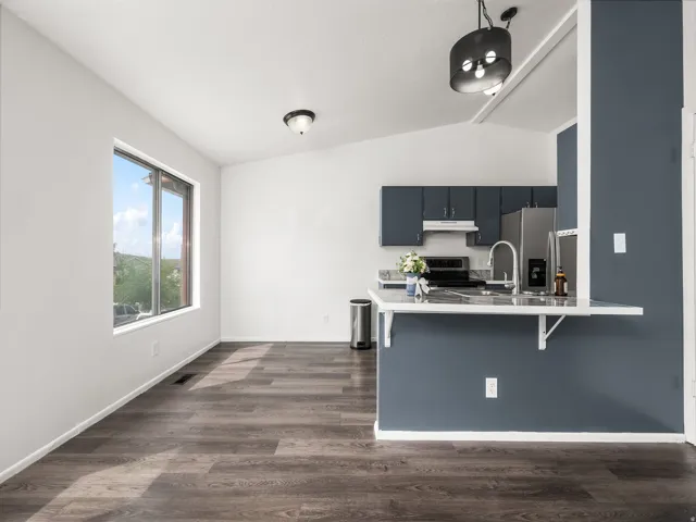 Open-concept space featuring wood-finish flooring, a kitchen island with seating, dark cabinetry, and a window with exterior views