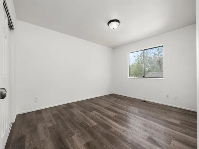 Room featuring wood-finish flooring, a contemporary flush-mount ceiling light, white walls, and a window with a dark frame