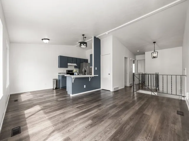 Open-concept living area featuring wood-finish flooring, vaulted ceilings, and a kitchen with deep blue cabinetry, stainless steel appliances, and a breakfast bar