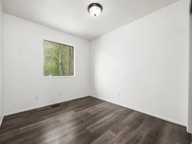 Bright room featuring a window overlooking natural scenery, wood-finish flooring, white baseboards, and a semi-flush mount ceiling light