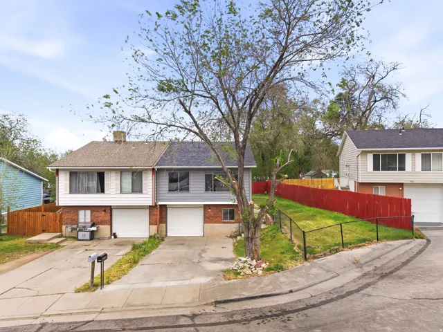 Duplex residence featuring brick and siding exterior, individual two-car garages, and separate paved driveways