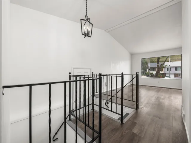 Upper-level landing featuring wood-finish flooring, a contemporary black metal chandelier, white walls, and a large window
