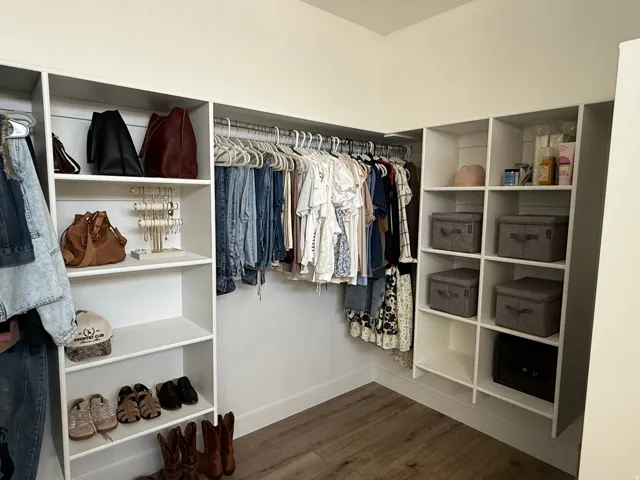 Custom closet system featuring white shelving units, multiple hanging rods, and wood-finish flooring