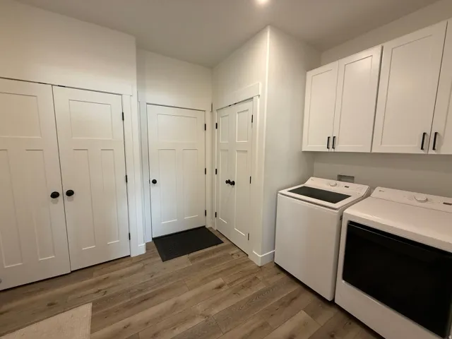 Utility area featuring wood-finish flooring, white shaker-style cabinetry with black hardware, and two white appliances
