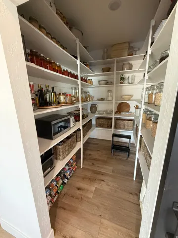Walk-in pantry featuring extensive white shelving, recessed lighting, wood-finish flooring, and a built-in can rack