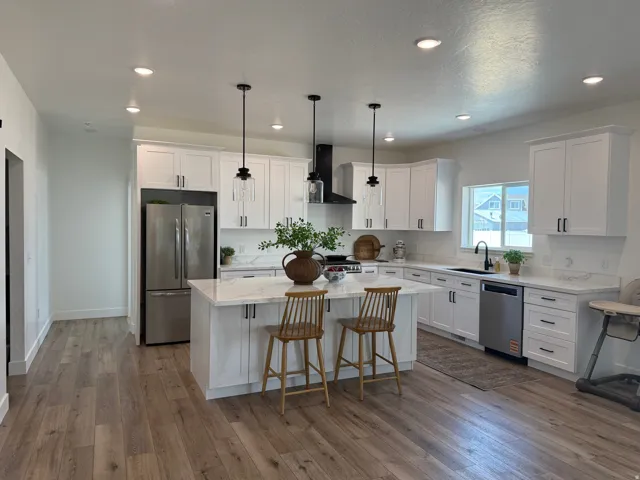 Modern kitchen featuring white shaker cabinetry with black hardware, stainless steel appliances, a center island with countertop seating, and wood-finish flooring