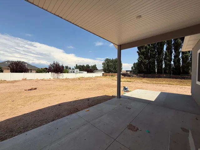 Spacious backyard featuring a concrete patio with an overhead cover, expansive open ground, and a perimeter fence