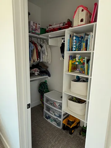 Built-in closet system featuring white shelving, hanging rods, and a textured grey carpet